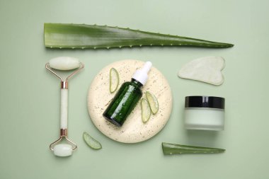 Kozmetik ürünlerle düz konum ve soluk yeşil arkaplanda aloe yaprakları kesimi