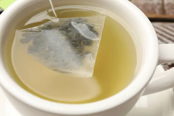 Tea bag in cup with hot drink on table, closeup