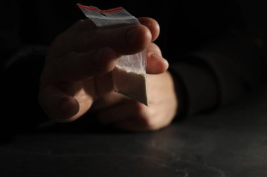 Uyuşturucu bağımlılığı. Gri masada plastik kokain torbası olan bir adam, seçici odaklı.