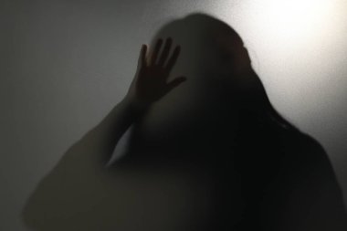 Camın arkasındaki hayalet silueti açık gri arkaplana karşı