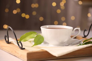 Fincanda romatik çay, çay tabağı, kaşık ve yeşil yapraklar masada.