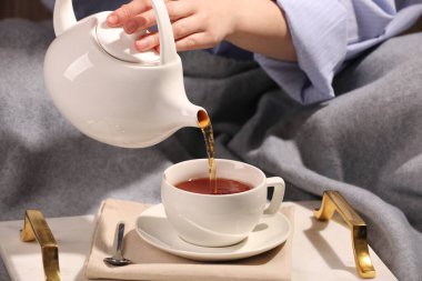 Kadın masadaki fincana aromatik çay dolduruyor, yakın plan.