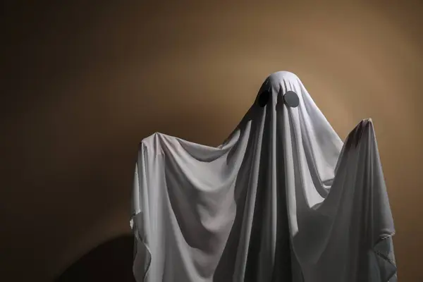 Creepy ghost. Woman covered with sheet on brown background, space for text