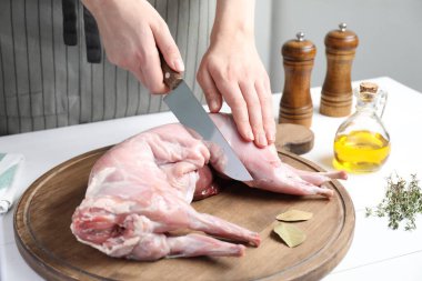 Beyaz ahşap masada bütün tavşanı kesen kadın, yakın plan.