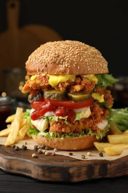 Çıtır tavuk köfteli lezzetli burger ve siyah ahşap masada patates kızartması, yakın plan.