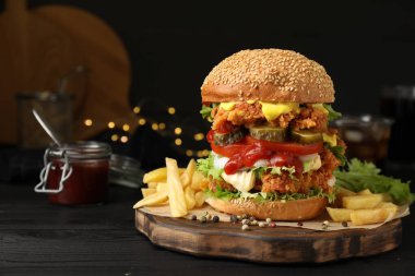 Çıtır tavuk köfteli lezzetli burger ve siyah ahşap masada patates kızartması.