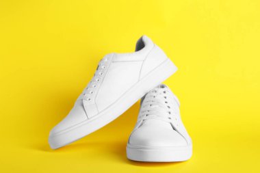 Sarı arka planda bir çift şık beyaz spor ayakkabı.