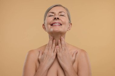 Güzel bir kadın bej arka planda boynuna dokunuyor.