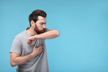 Hasta adam dirseğine açık mavi arka planda öksürüyor, mesaj için yer var. Soğuk belirtileri