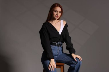 Gri arka planda taburede oturan güzel genç bir kadın.