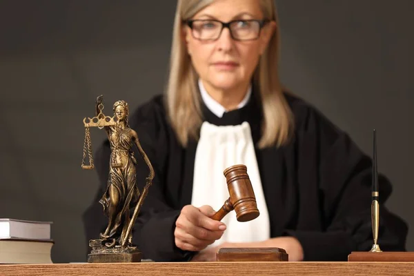 Judge striking mallet at wooden table, selective focus. Figure of Lady Justice indoors