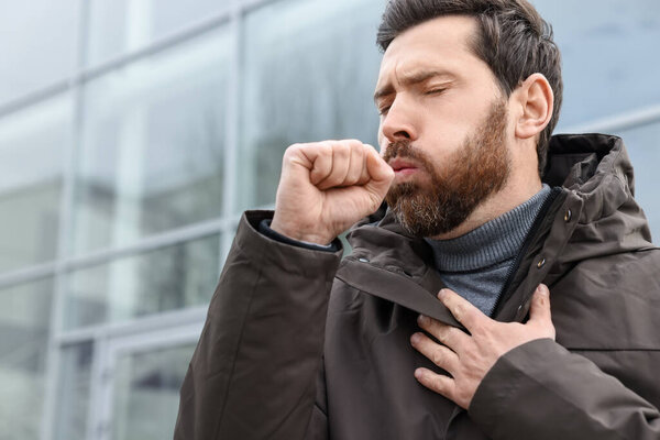 Sick man coughing on city street. Cold symptoms