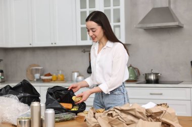 Çöp ayıklama. Mutfakta yemek artıklarını plastik torbaya koyan bir kadın.