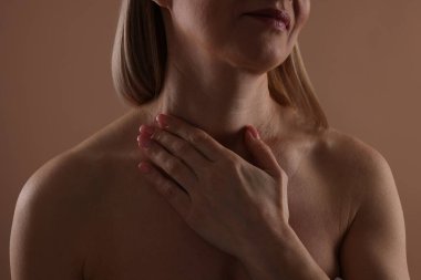 Güzel bir kadın bej arka planda boynuna dokunuyor, yakın plan.