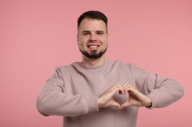 Pembe arka planda elleri olan bir adam kalp hareketi gösteriyor.