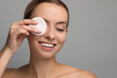 Gülümseyen kadın makyajı gri arka planda pamukla temizliyor, yakın plan. Metin için boşluk