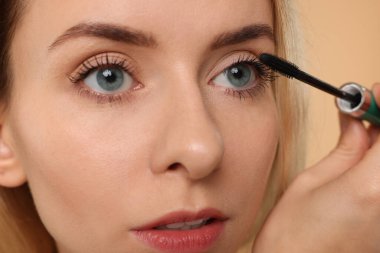 Güzel bir kadın bej arka plana rimel sürüyor, yakın plan.