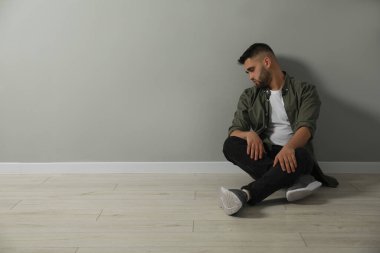 Açık gri duvarın yanında yerde oturan üzgün adam. Metin için boşluk