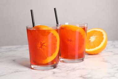 Aperol spritz kokteyli, portakal dilimleri ve beyaz mermer masa üzerinde pipetler.