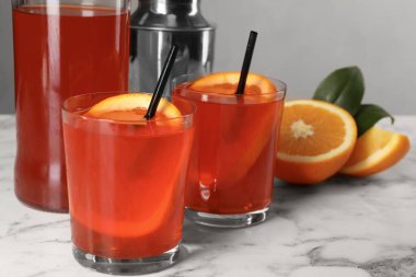 Aperol spritz kokteyli, portakal dilimleri ve pipetler beyaz mermer masada, yakın plan.