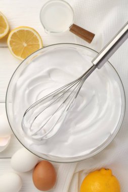 Krem şantili kase, çırpılmış çırpılmış ve malzemeler beyaz ahşap masada, düz yatıyordu.