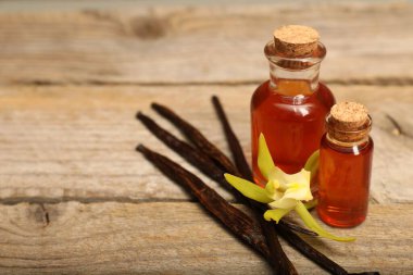 Aromatik vanilya özü, kapsüller ve çiçek ahşap masada, yakın plan. Metin için boşluk