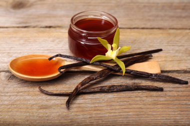 Aromatik vanilya özü, kapsüller ve çiçek ahşap masada.