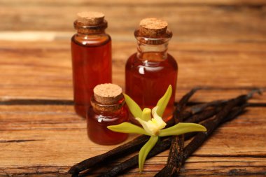 Aromatik vanilya özü, kapsüller ve çiçek ahşap masada, yakın plan.