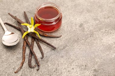 Aromatik vanilya özü, kapsüller ve çiçekler gri masada. Metin için boşluk