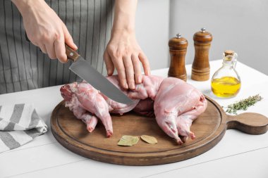 Beyaz ahşap masada bütün tavşanı kesen kadın, yakın plan.