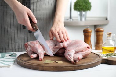 Beyaz ahşap masada bütün tavşanı kesen kadın, yakın plan.