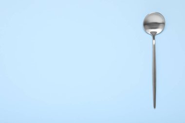 Açık mavi arka planda parlak gümüş bir kaşık, üst manzara. Metin için boşluk
