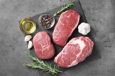 Çiğ biftek, yağ ve baharatlar gri arka planda, üst manzara