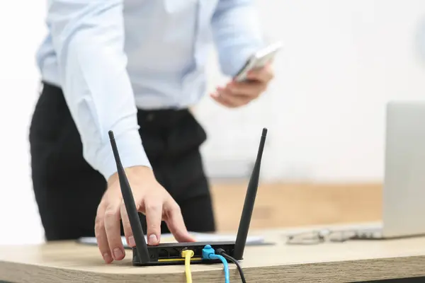 Man inserting cable into Wi-Fi router at wooden table indoors, closeup. Space for text