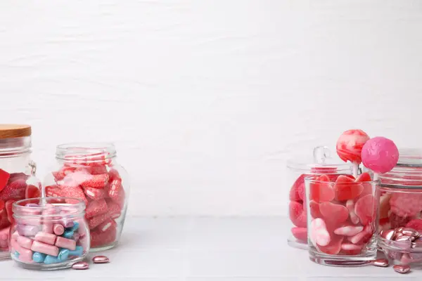 Tasty pink candies in glass jars on white background, space for text