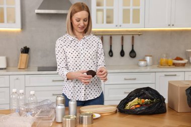 Mutfaktaki çöpleri ayıran gülümseyen kadın.