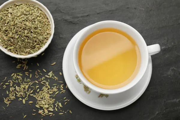 Aromatic fennel tea in cup and seeds on black table, flat lay
