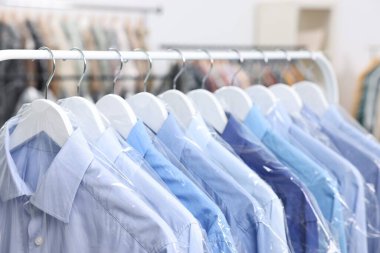 Kuru temizleme servisi. Plastik poşetlerdeki birçok farklı giysi kapalı yerlerde asılı, yakın plan.