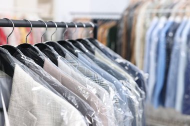Kuru temizleme servisi. Plastik poşetlerdeki birçok farklı giysi kapalı yerlerde asılı, yakın plan.