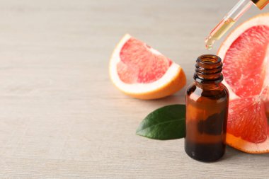 Pipetten şişeye greyfurt yağı damlatıyor ve açık ahşap masaya taze meyve döküyor, yakın plan. Metin için boşluk