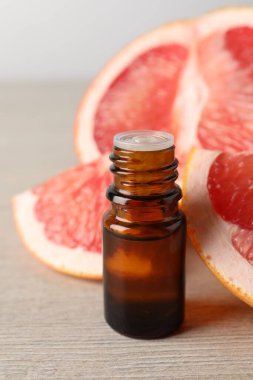 Şişede greyfurt yağı ve açık ahşap masada meyve, yakın plan.