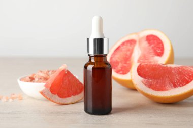 Şişede greyfurt yağı ve açık ahşap masada meyve, yakın plan.