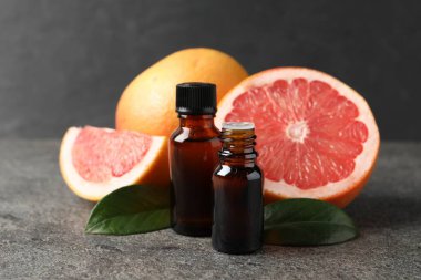 Şişelerdeki greyfurt yağı, yapraklar ve meyveler koyu dokulu masa üzerinde, yakın çekim