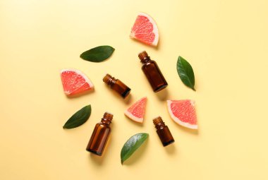 Şişelerde greyfurt yağı, yapraklar ve sarı masada meyve kesimi.