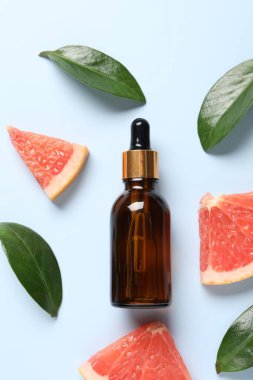 Şişede greyfurt yağı, yapraklar ve açık mavi masada meyve kesimi, düz uzanma