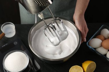 Siyah masada el çırpıcı ile krem şanti yapan kadın, yakın plan.