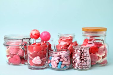 Cam kavanozlarda açık mavi arka planda lezzetli pembe şekerler.