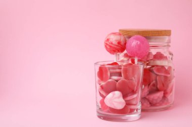 Pembe arka planda cam kavanozlarda lezzetli şekerler, metin için yer