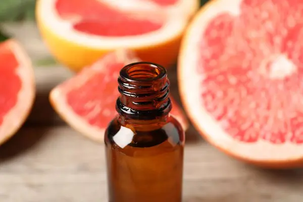 Grapefruit essential oil in bottle and fruits on table, closeup