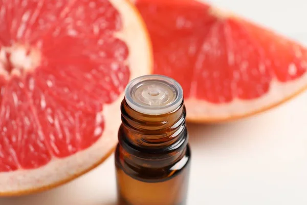 Grapefruit essential oil in bottle and fruit on white table, closeup